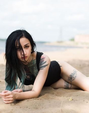 Petite brunette cam girl with amazing tattooes on her whole body lying in the sand